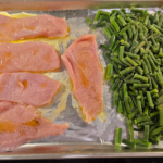 Organic chicken thighs and frozen green beans arranged on a sheet pan ready for roasting