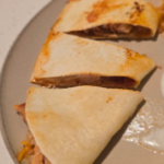 Chicken quesadillas cut into triangles on a plate with sour cream